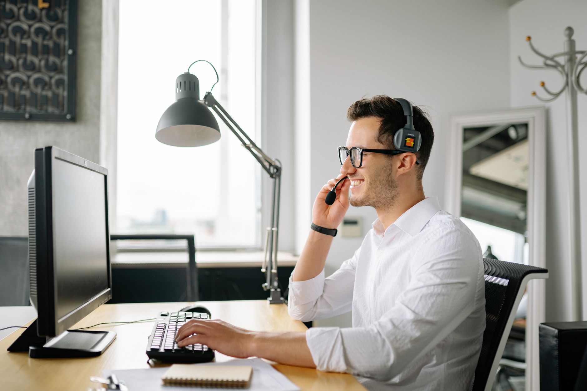 Smiling man wearing headset working at computer in bright office — illustrating: How to Evaluate Managed VoIP Providers in Central Florida Without Getting Locked Into Bad Contracts